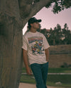 Person wearing a graphic t-shirt leaning against a tree in an outdoor setting