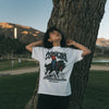 Person wearing a 'Cowgirl' t-shirt with a graphic design, standing next to a tree in an outdoor setting.