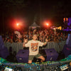 DJ performing at a music festival with crowd and stage lights in the background