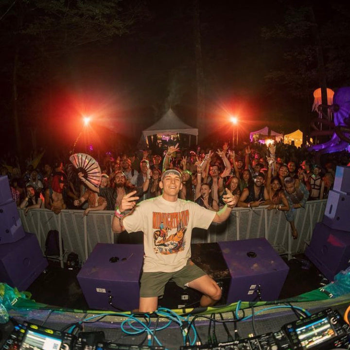DJ performing at a music festival with crowd and stage lights in the background